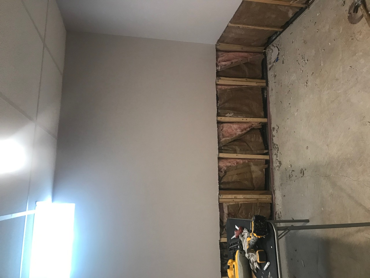Wall stripped back to the bare studs and concrete, ready for new insulation and drywall.